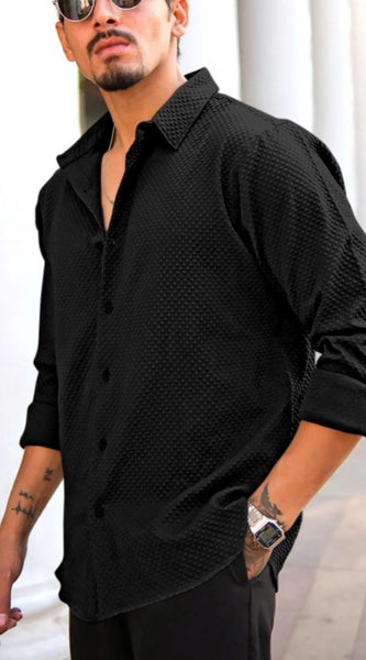 Man wearing a black textured shirt with rolled-up sleeves in an urban setting.